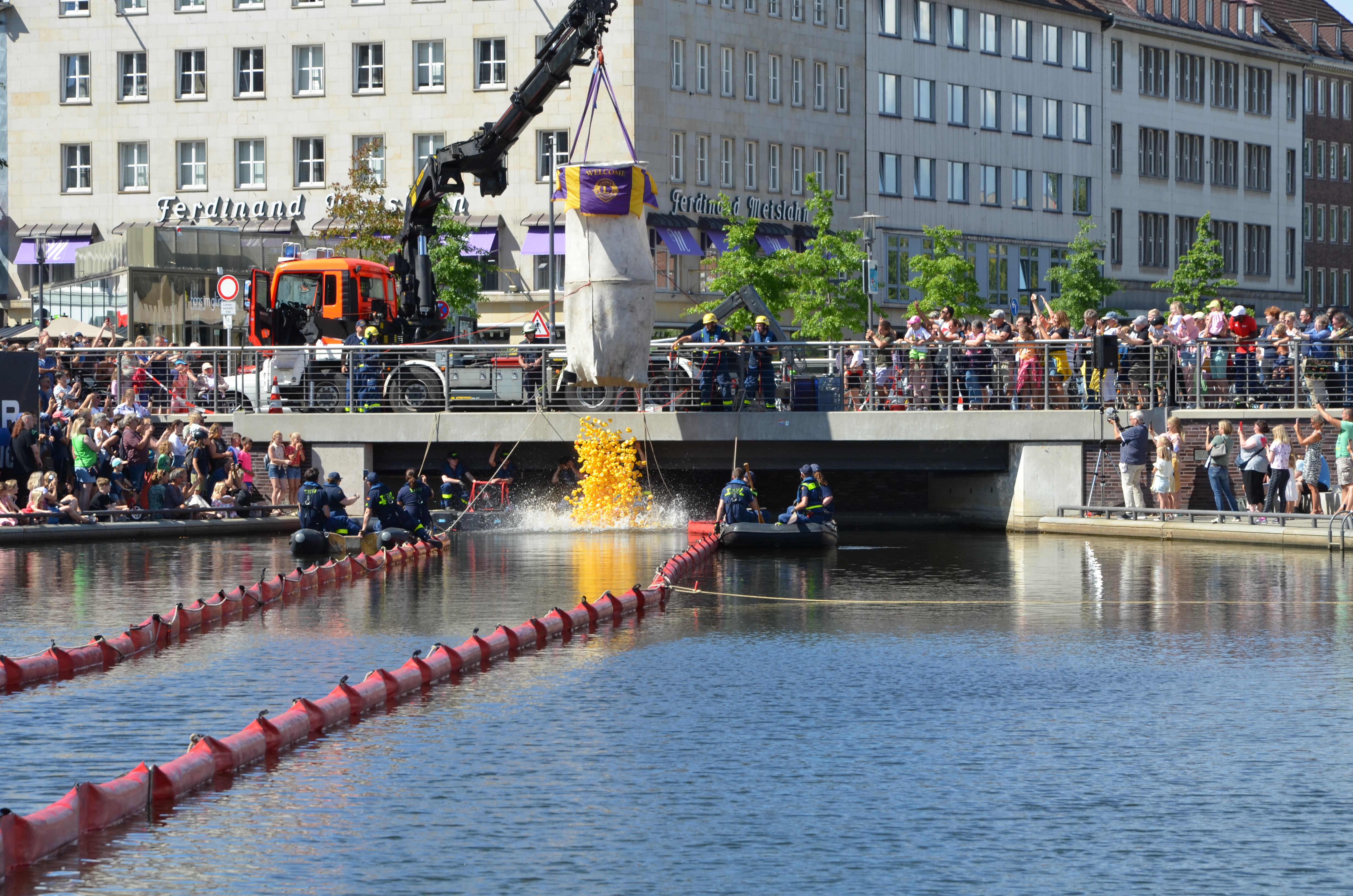 Ein Kran hebt den Sack voller Badeenten über den Bootshafen und tausende Enten fallen ins Wasser